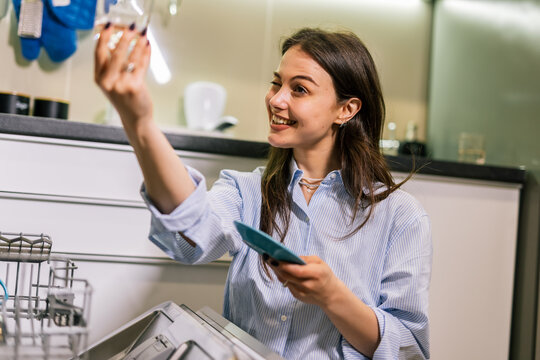 Young woman unloading dishwasher in modern kitchen - Powered by Adobe