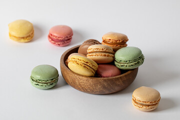 Macarons of different colors and flavors in a wooden bowl on a white background