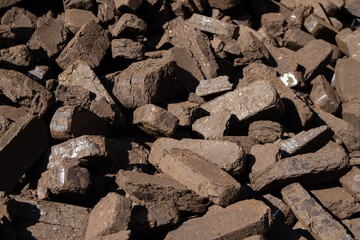 Large chunks of coal stacked together at a mining site show different shapes and textures under bright sunlight, emphasizing natural resources