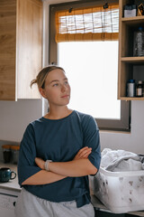 Laundry basket and coffee mug in a cozy home scene with a young woman in loungewear taking a break from housework; domestic life concept, candid indoor lifestyle background with copy space.