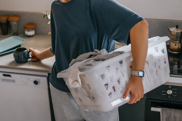 Laundry basket and coffee mug in a cozy home scene with a young woman in loungewear taking a break from housework; domestic life concept, candid indoor lifestyle background with copy space.