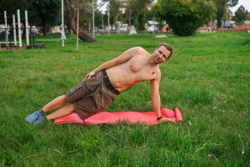 Man doing side plank exercise outdoors on green grass
