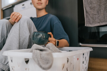 Laundry basket and coffee mug in a cozy home scene with a young woman in loungewear taking a break from housework; domestic life concept, candid indoor lifestyle background with copy space.
