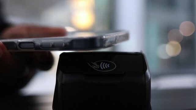 Customer is using a mobile phone to make a payment at a terminal, showcasing the simplicity and convenience of contemporary electronic and wireless payment methods in stores