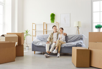 Couple sitting on sofa amid boxes in apartment. They pause during moving to enjoy a calm moment,...