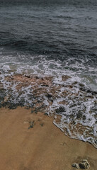 High-angle view of moody dark waves crashing onto the unique orange-brown sand and mossy rocks of Dato Beach, Majene, West Sulawesi. A perfect texture and pattern for coastal and abstract themes.