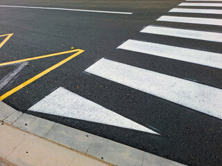 New pedestrian crossing markings on fresh asphalt road surface in urban area near busy street intersection