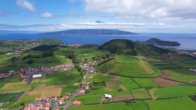 AZORES - 10.27.2025 - Great aerial footage traveling over Faial Island's green hills, headed towards the water with a view of a Pico Island volcano in the distance.