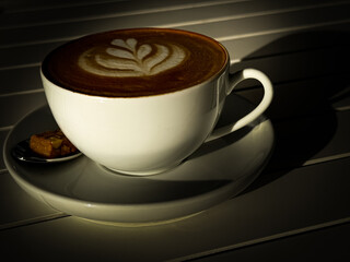 A cup of cappuccino on a white wooden table in the shadows