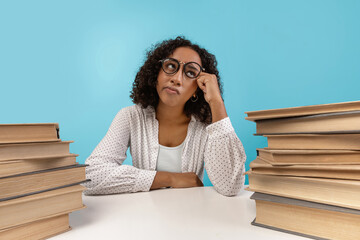 A young black female student sits at a desk with piles of books, daydreaming and feeling bored during a college lesson. The blue background highlights her disengagement.