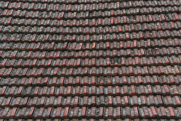 Close-up view of an old roof covered with weathered red clay tiles arranged in neat horizontal rows. Weathered red clay tiles with dirt and aged texture