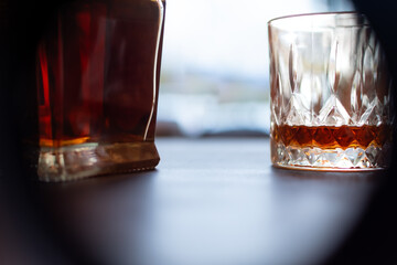 High-contrast minimalist shot of whiskey bottle and glass framed by dark edges against bright blurred background. Modern product concept with copy space