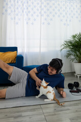 Man training at home on a mat, performing a lateral leg raise while his cute pet plays beside him. Concept of home workout, well being, and active lifestyle