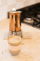 a flat white coffee in a pottery mug, with the copper moka pot  in the background