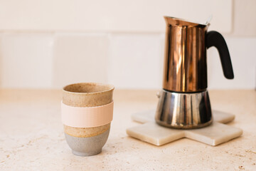 a flat white coffee in a pottery mug, with the copper moka pot  in the background