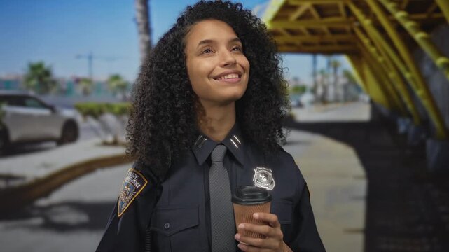 Young woman police officer smiling outdoors holding coffee on street in uniform