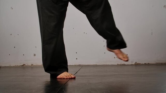 Close up of the legs of a man practicing Wing Chun in a black kimono, demonstrating his skills against a gray studio backdrop, showing self defense training and martial arts techniques.