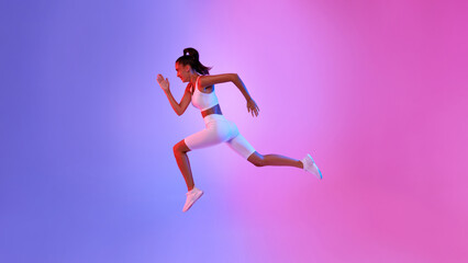 Fototapeta premium Happy fit lady is jumping in mid-air while exercising against a neon pink and blue background. She wears white sportswear and showcases her enthusiasm for fitness in a studio setting.