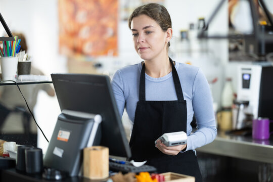 Young female cashier in apron at cash register in cafe