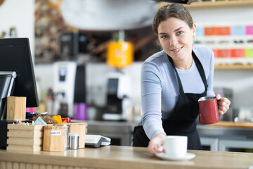 Positive female cafe employee pours coffee for cafe customers