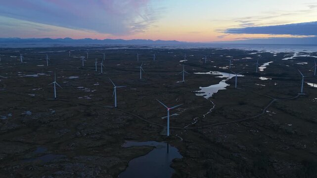 Wind towers stretch across countryside at dusk, aerial clean energy