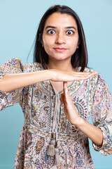 Indian person doing the time out symbol to ask for pause or work break, feeling tired and frustrated against blue background. Young woman with burnout asking for a break in studio.