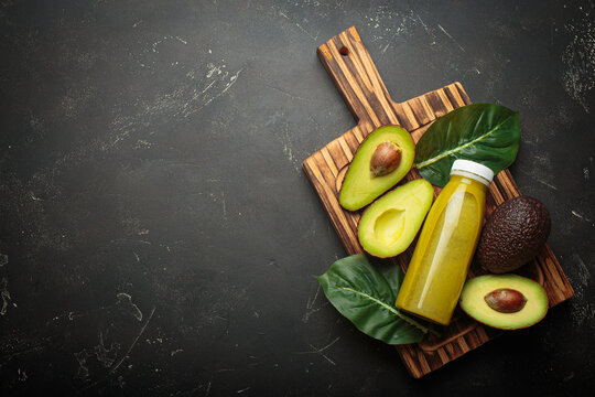 Vibrant green avocado smoothie in a plastic bottle with sliced avocados and a green leaf on a dark background copy space