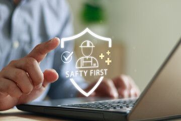 Businessman using laptop and touching digital “Safety First” icon with shield and worker symbol, representing workplace safety, health protection and industrial security management in modern business.