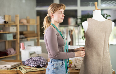 Female dressmaker works with a dress on a mannequin, she checks the dimensions and quality of the...