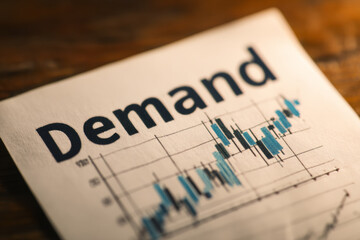 Obraz premium The word demand made of wooden blocks placed on financial charts, symbolizing market analysis and economic trends.