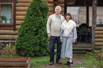 Fototapeta premium Village couple pensioners posing near a log bathhouse.