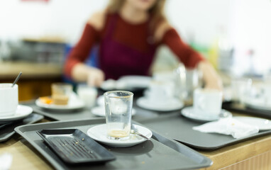 Young female waitress in apron collects dirty cups and plates in cafe
