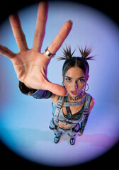 Stylish woman in punk Y2K fashion reaching for the camera in a high angle fisheye portrait. Edgy youth with spiky pigtails and bold makeup under vibrant blue and purple studio lights