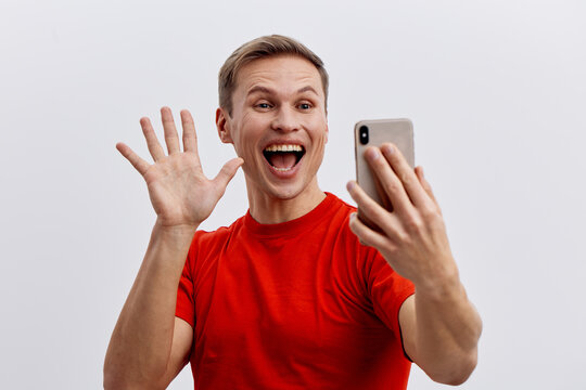 cheerful young caucasian man video calling use smartphone in red t-shirt isolated on gray background digital communication concept