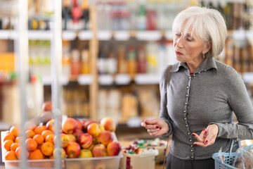 Elderly woman buyer with basket of food choosing products in grocery store