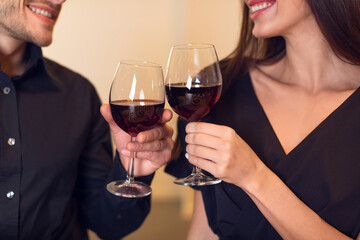 A couple raises their glasses of red wine, sharing a joyful toast. They are dressed elegantly, celebrating a romantic occasion. The atmosphere is warm and intimate, enhancing their connection.