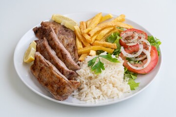Sliced pork rice fries salad lemon, herbgrilled pork slices served with fluffy rice, crispy fries, tomato and onion salad, lemon wedge and parsley, wholesome family lunch