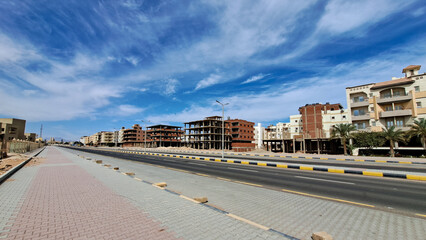 Fototapeta premium Urban landscape featuring modern architecture and construction sites alongside a wide road, showcasing a vibrant city development under a clear blue sky. Hurghada, Egypt, Red Sea