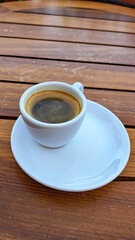 Espresso coffee served in a white ceramic cup on a round plate, placed on a wooden table, showcasing rich texture and inviting aroma of freshly brewed beverage