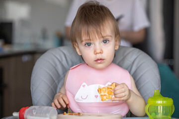 Infant girl eats deliciously while sitting at a childrens table