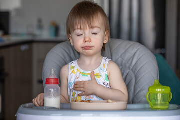 Infant girl eats deliciously while sitting at a childrens table