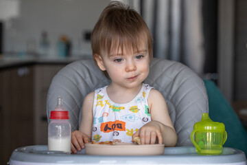 Infant girl eats deliciously while sitting at a childrens table