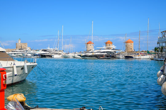 Fishing boats and yachts line the Mandraki Harbor with the historic windmills and lighthouse, site of the ancient Colossus on the island of Rhodes, Greece.