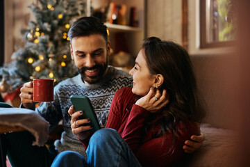 Happy couple using smart phone while spending Christmas at home.