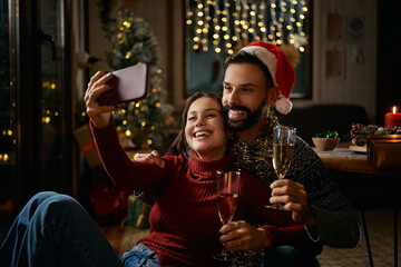 Festive couple taking selfie while drinking champagne on New Year's Eve.