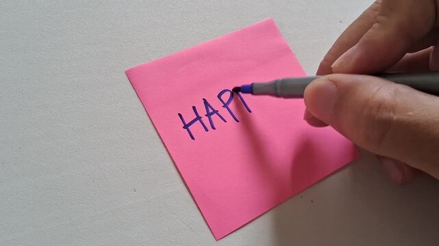 Writing a message of HAPPY on a pink post-it note