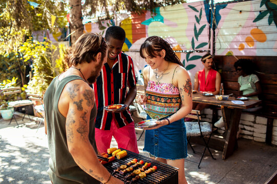 Young adults laughing while grilling at backyard garden party