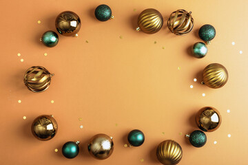 Golden and green Christmas baubles forming a circular frame with confetti on a warm orange background. Top view, flat lay, copy space