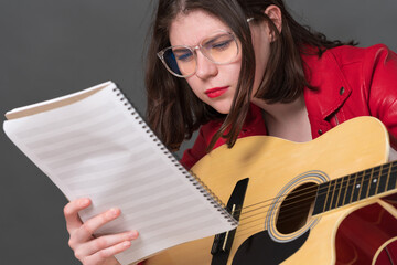 Closeup view of female guitarist in glasses studying sheet music as she is learning to play guitar