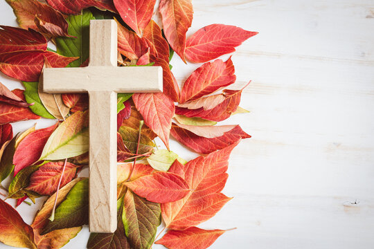 Wood cross on autumn leaves on a white wood background with copy space